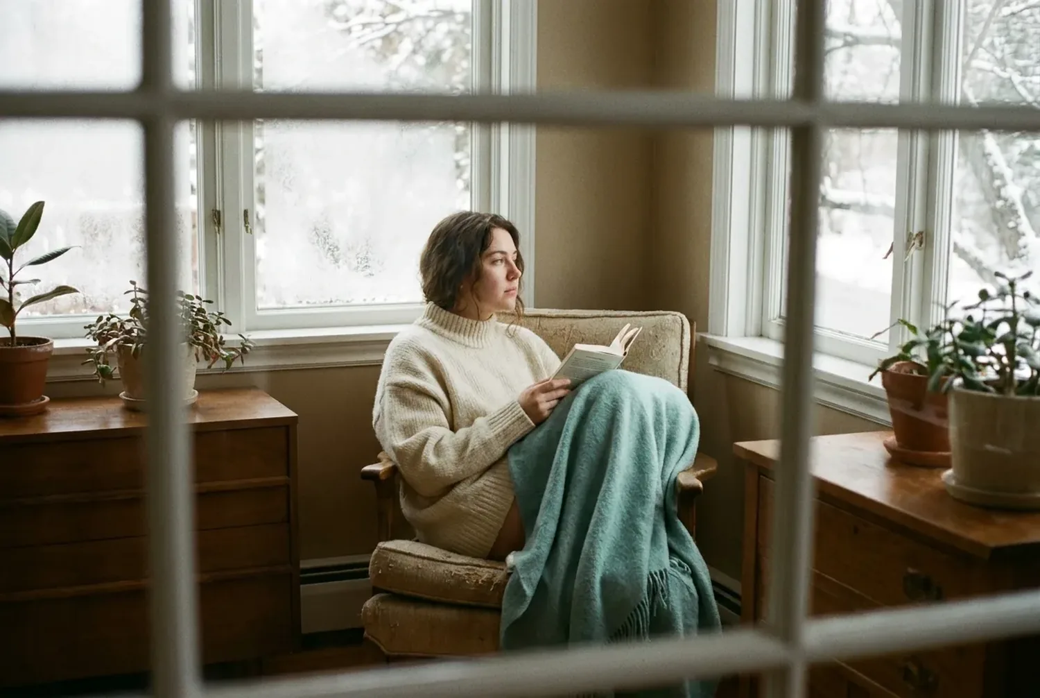 A person wrapped in a soft sweater reading quietly by a window in low winter morning light