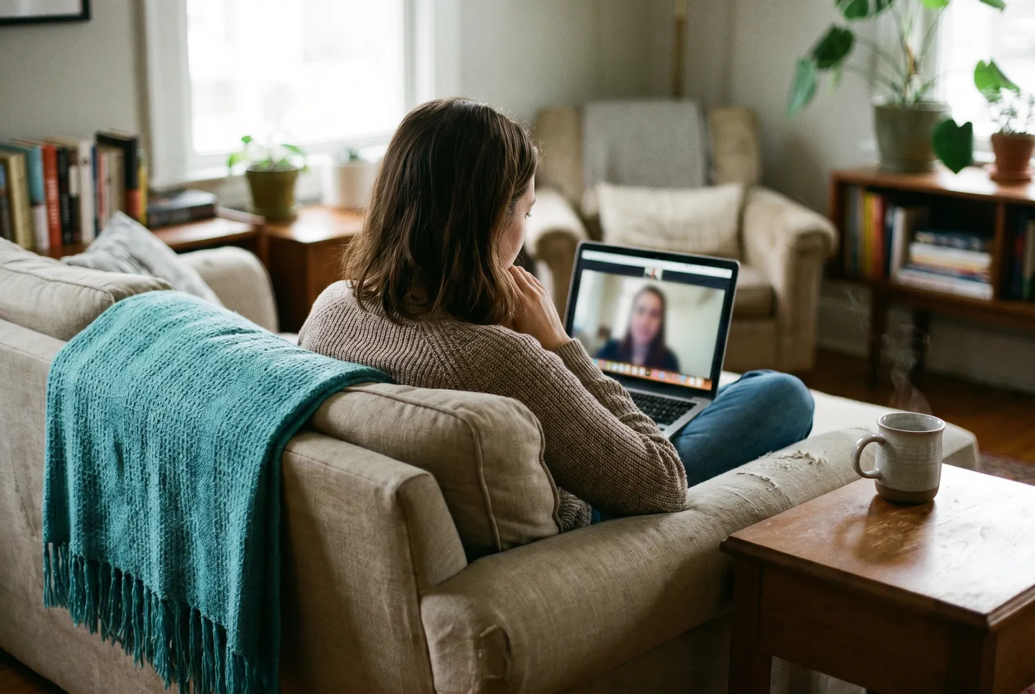 Woman on a sofa attending a telepsychiatry video appointment on her laptop
