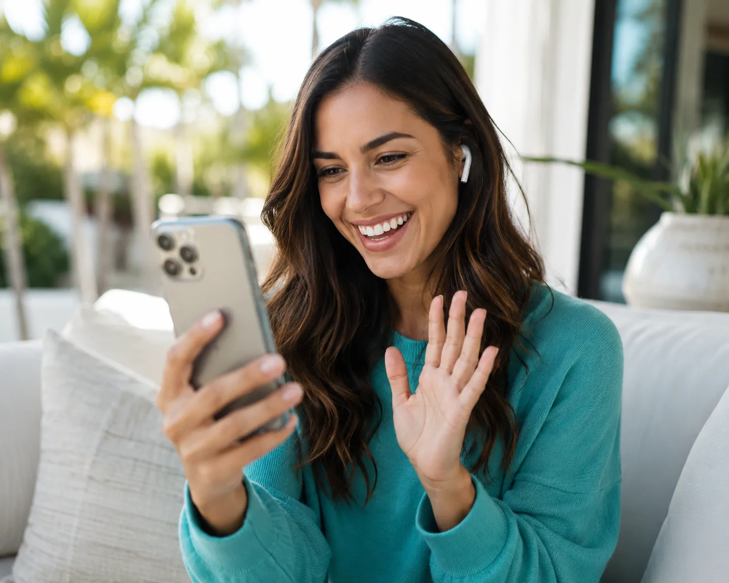 A smiling woman in a teal sweater waves to her psychiatrist during a phone video visit from her sunny patio A smiling woman in a teal sweater waves to her psychiatrist during a phone video visit from her sunny patio
