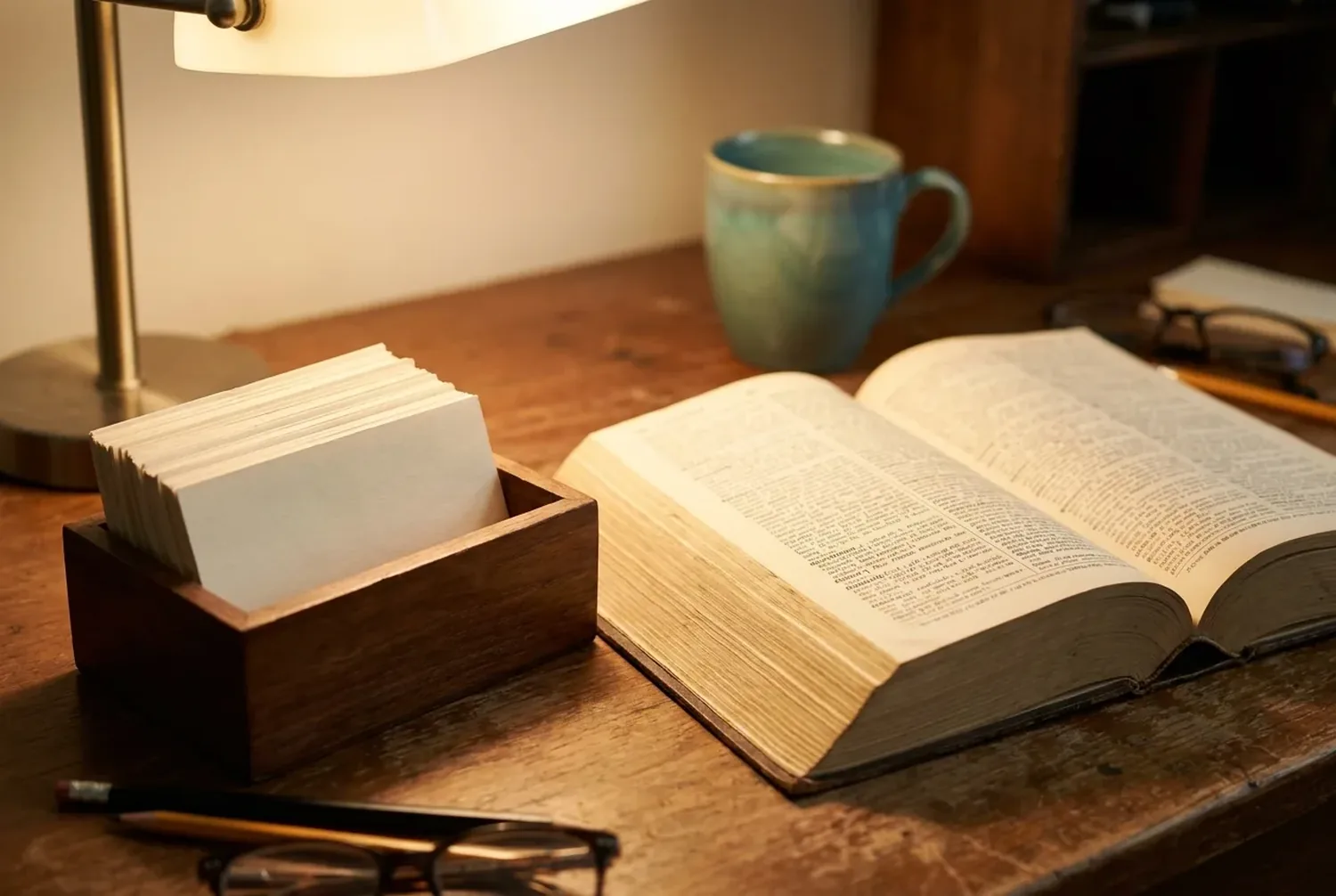 An open dictionary beside a small box of neatly arranged index cards on a wooden desk in warm light An open dictionary beside a small box of neatly arranged index cards on a wooden desk in warm light