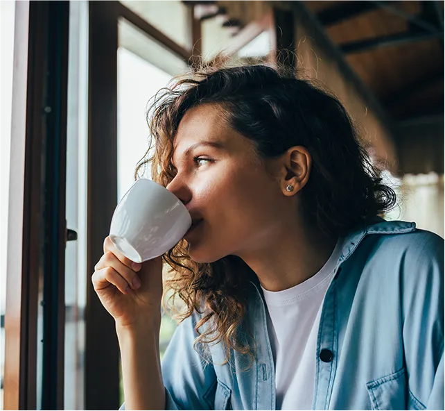 woman drinking coffee looking outside window