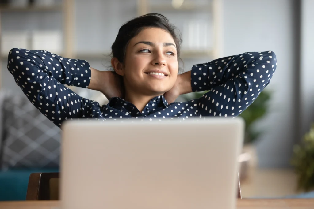 Woman leaning back in chair and looking up from laptop