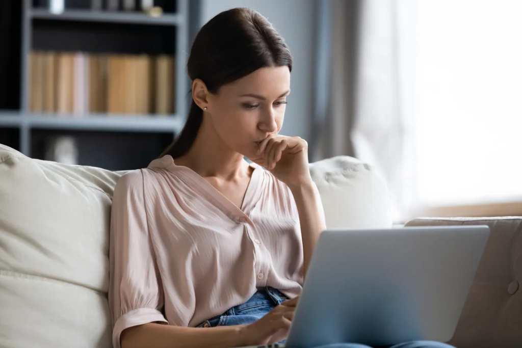 woman sitting down while focused on laptop screen on her lap