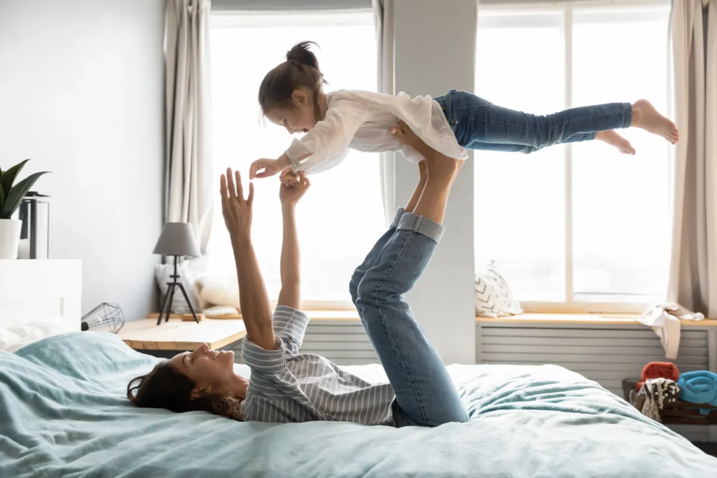 woman on her back with feet up in the air joyfully holding her child