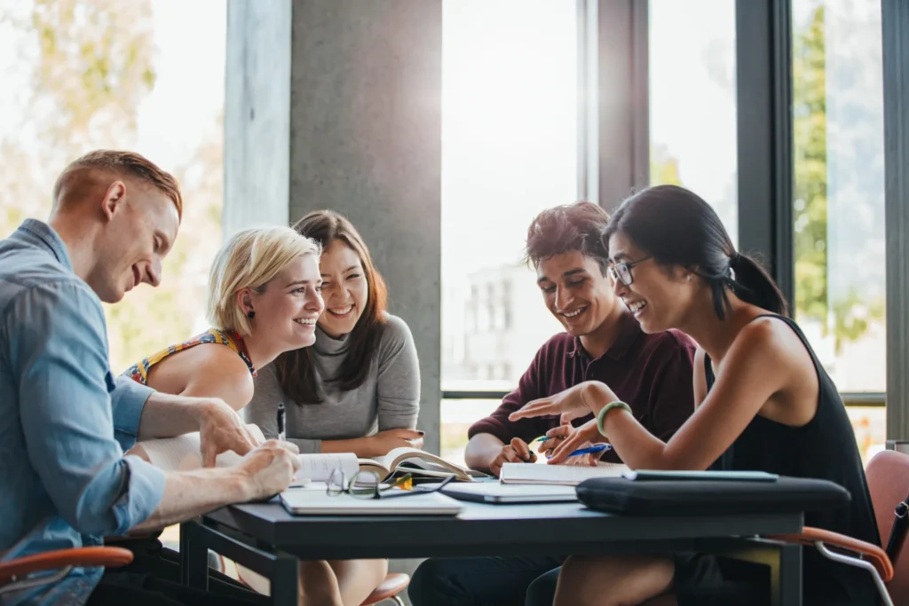 group of students sitting at a table smiling with books in front of them