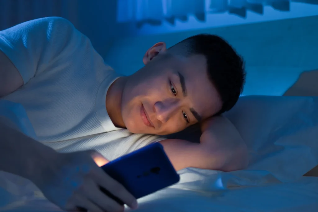 man laying down while looking at phone in the dark