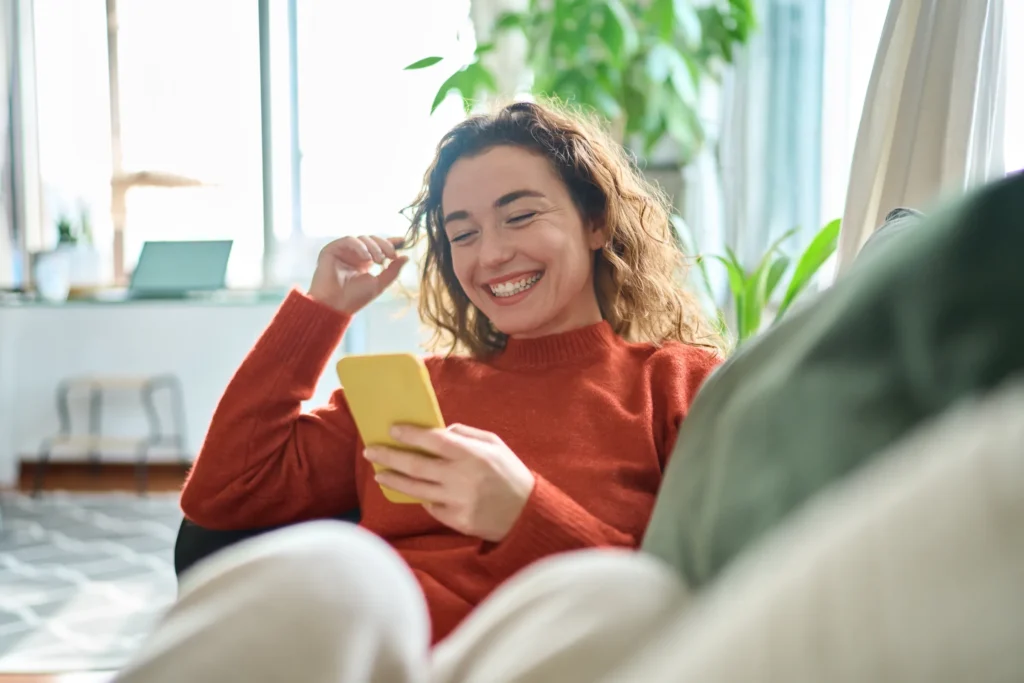 woman sitting on couch smiling and looking at her phone