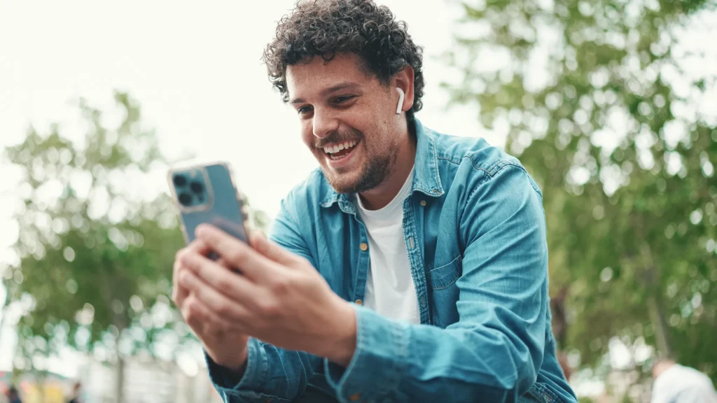 man sitting outdoors smiling and looking at phone