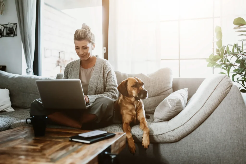 woman sitting on couch with laptop and dog at her side