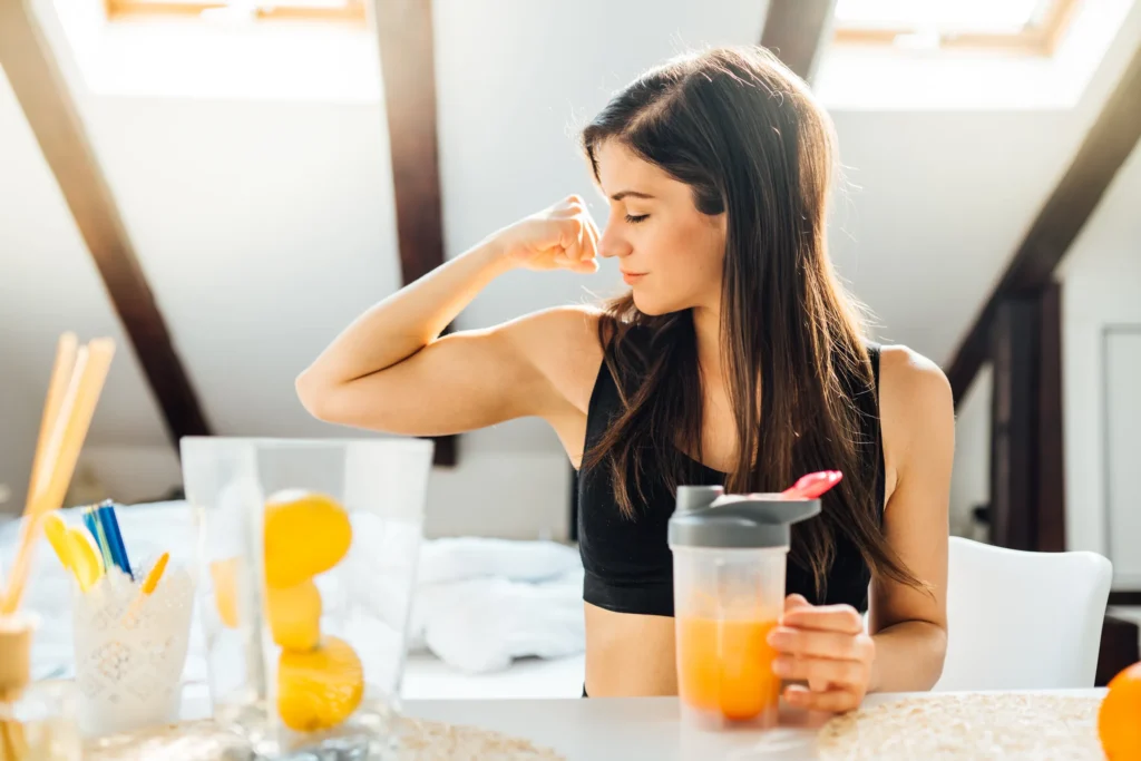 woman flexing bicep with smoothie making materials in front of her