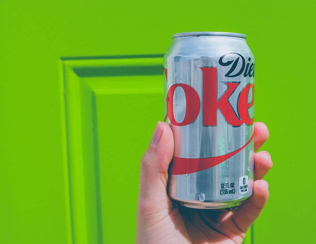 A hand holding a can of diet soda, highlighting how beverages can influence eating habits and mental health.
